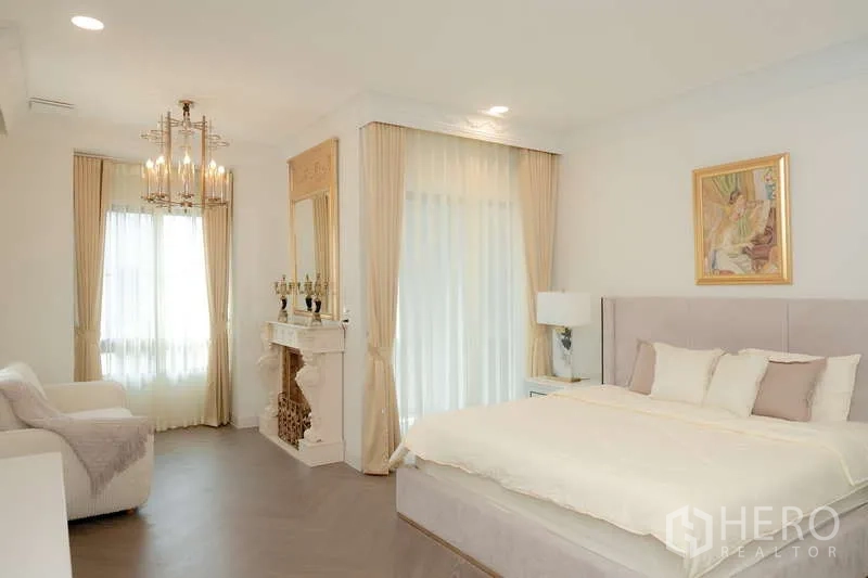 Detached House for rent or sale in Saphan Sung, Bangkok - Bright master bedroom with chandelier, decorative fireplace, large windows and an upholstered bed.