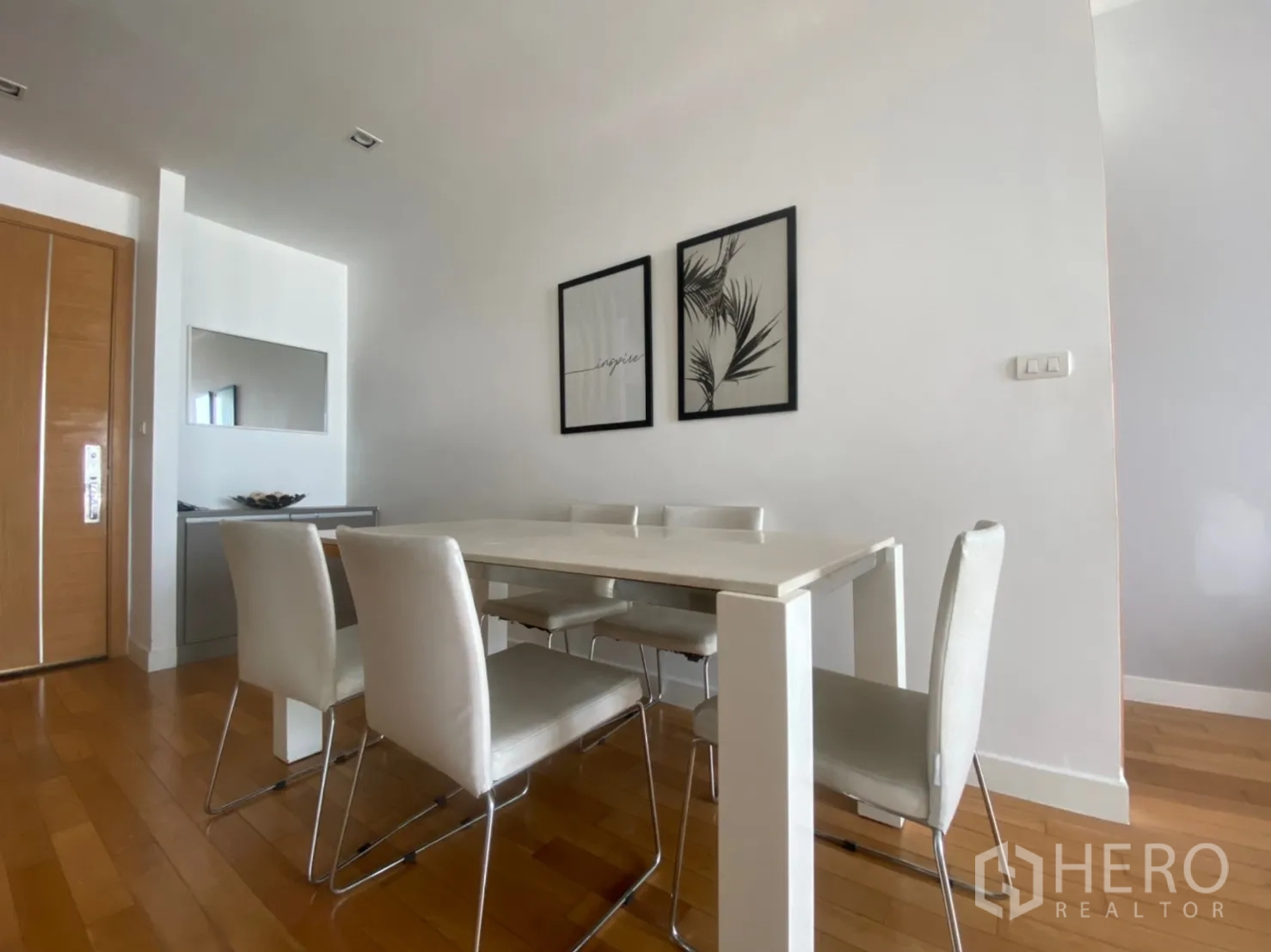 Condominium for rent or sale in Khlong Toei, Bangkok - Minimalist dining corner with white table and chairs beside the entry and wall art.
