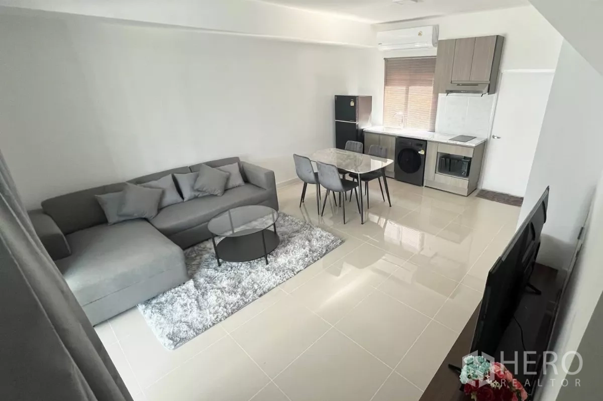 Townhouse for rent in Bang Phli, Samut Prakan - Open-plan living, dining and built-in kitchen with gray sofa, dining set, refrigerator, oven and washer.