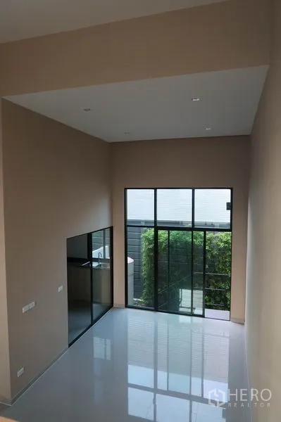 Townhouse for rent in Suan Luang, Bangkok - Double-height living area of a modern Suan Luang townhouse with floor-to-ceiling windows and glossy tile floors.