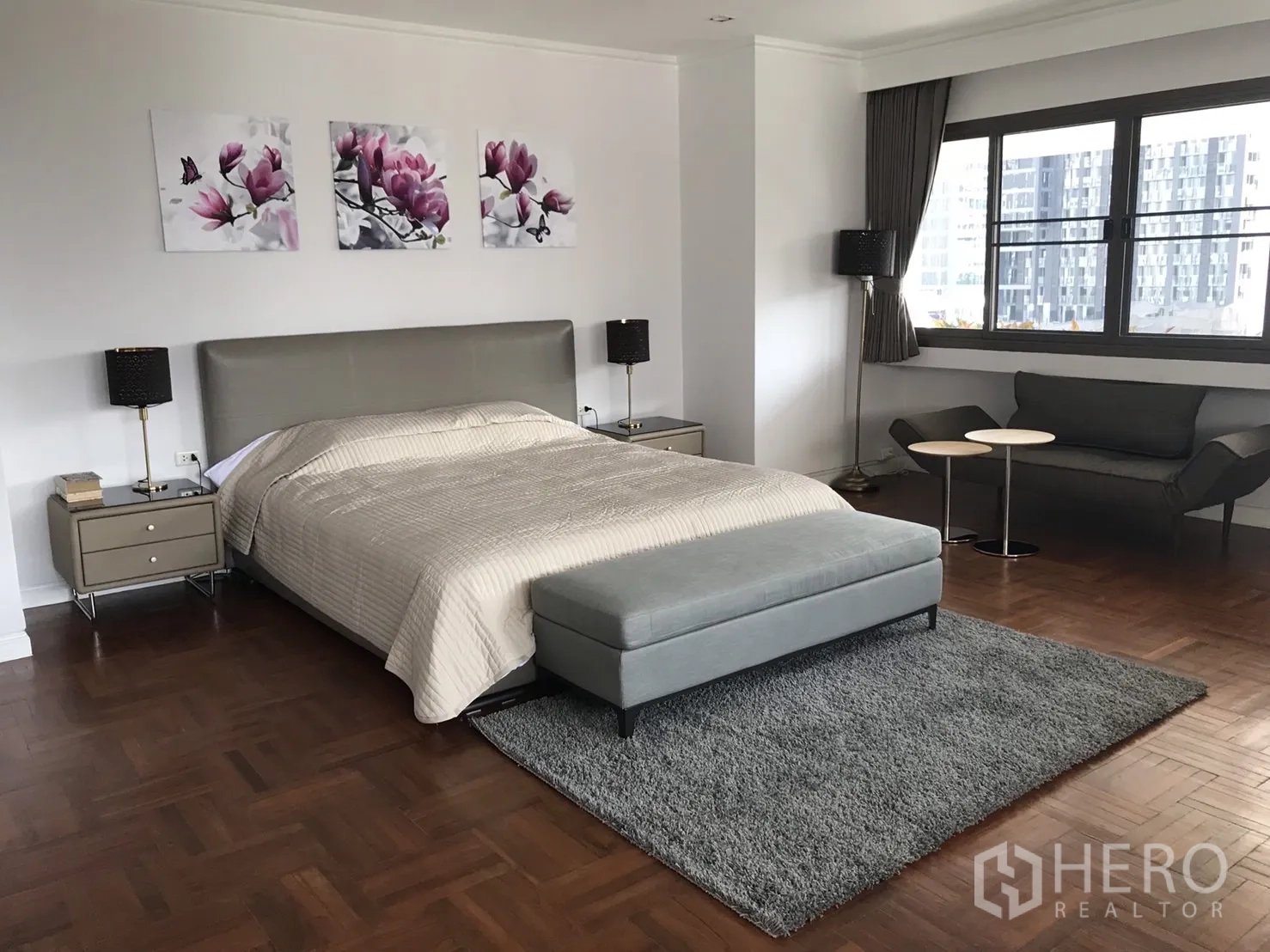 Condominium for rent in Bangkok - Expansive master bedroom with seating area, bench and city views from wide windows.