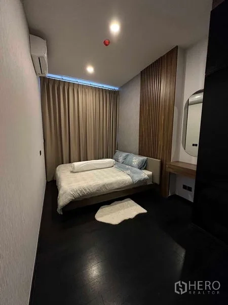 Condominium for rent in Khlong Toei, Bangkok - Cozy bedroom with double bed, wood slat accent wall, vanity and blackout curtains.
