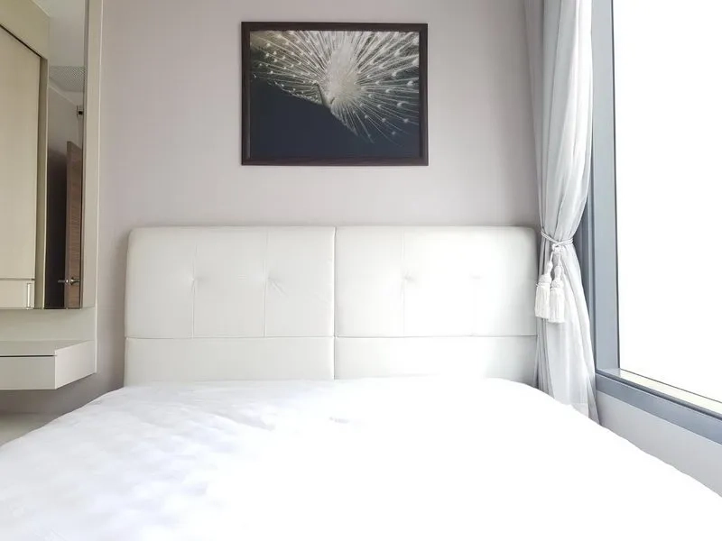 Condominium for rent in Ratchathewi, Bangkok - Bright bedroom with a white upholstered headboard and large window with sheer curtains.