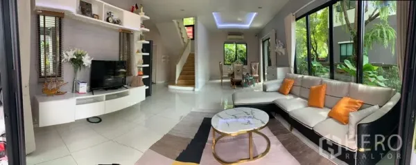 独立式住宅 出租在Bang Phli, Samut Prakan - 采光充足的客厅，转角沙发、电视柜与大理石茶几，落地窗望向花园景色