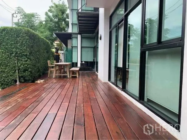 带办公室的家 出售在Wang Thonglang, Bangkok - 宽敞木质露台，旁有修剪整齐的绿篱和落地窗，配户外桌椅