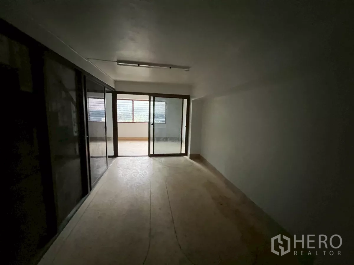 Shophouse for rent in Khlong Toei, Bangkok - Long upper-level room with sliding glass doors opening to an enclosed balcony area.