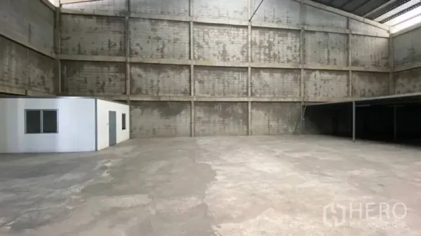Warehouse for rent in Prawet, Bangkok - Wide view of high-bay warehouse showing concrete floor, left-side office box, and right-side mezzanine structure.