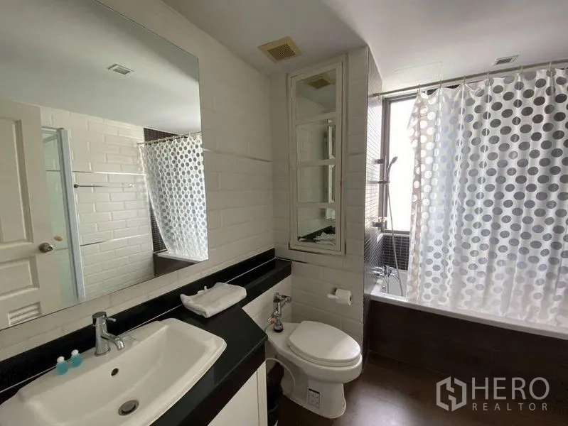 Condominium for rent in Khlong Toei, Bangkok - Modern bathroom with vanity, toilet, and a shower-over-bathtub with window.