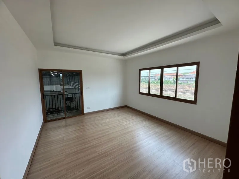 Warehouse for rent in Lam Luk Ka, Pathum Thani - Upstairs room with wood-look flooring, large window and sliding door to a balcony.