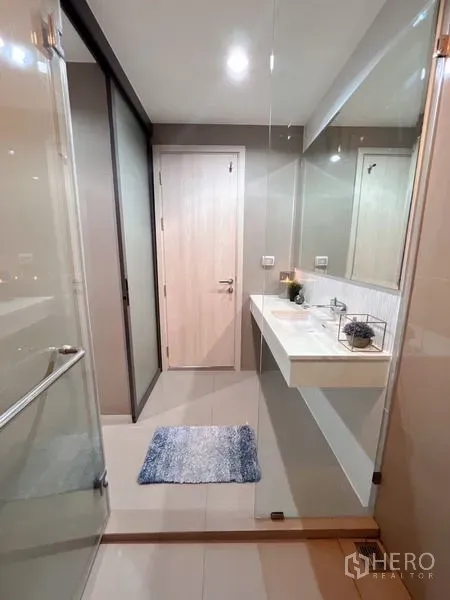 Condominium for rent or sale in Khlong Toei, Bangkok - Bathroom view from shower showing vanity, door and clear glass partition.