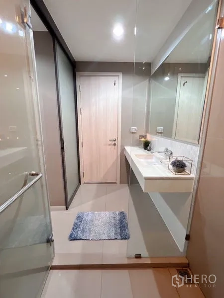 Condominium for rent or sale in Khlong Toei, Bangkok - Bathroom view from shower showing vanity, door and clear glass partition.
