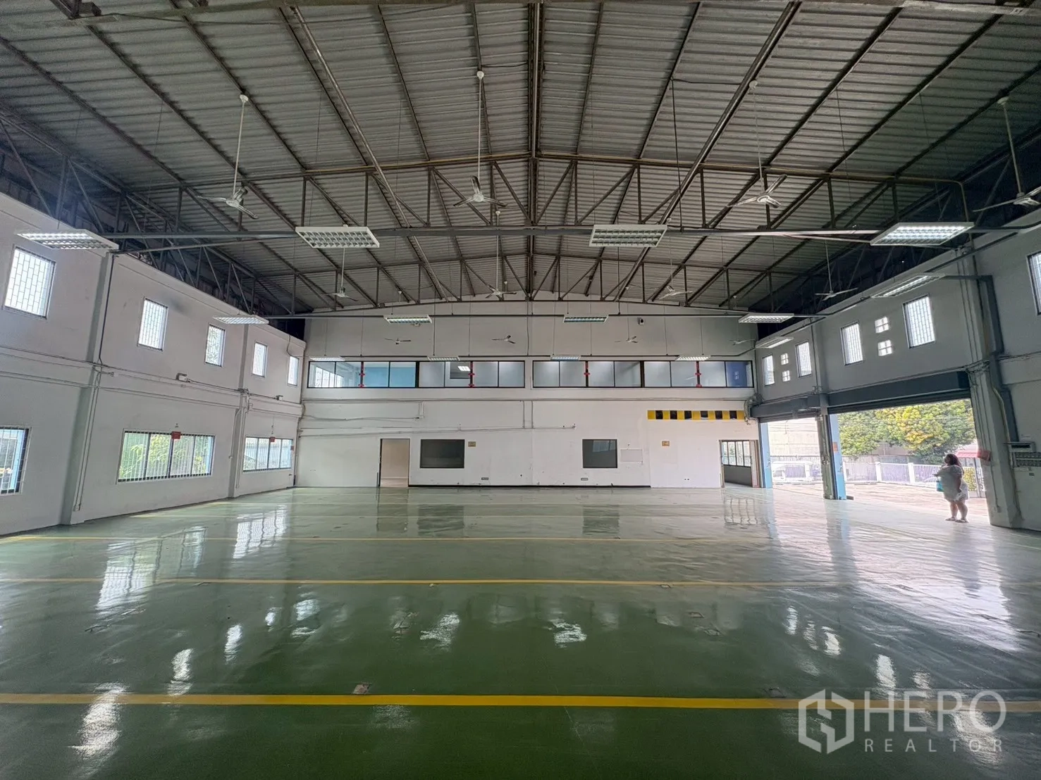 Warehouse for rent in Phra Khanong, Bangkok - Bright industrial hall featuring steel truss roof, glass‑block windows, and polished green floor.