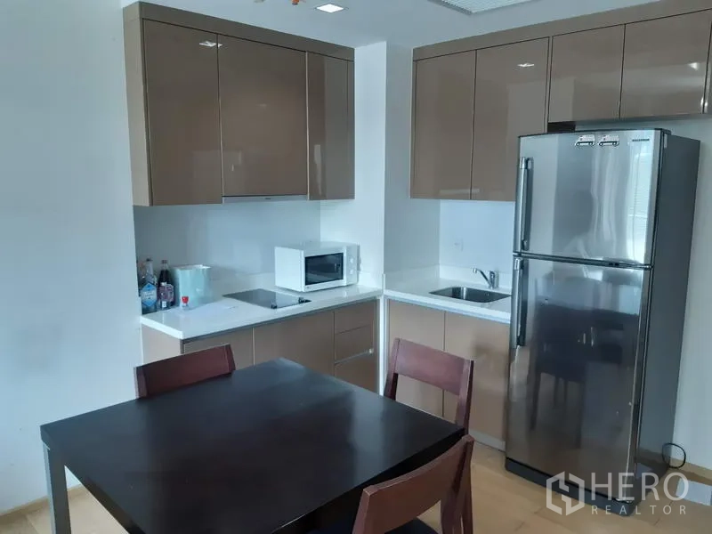 Condominium for rent in Khlong Toei, Bangkok - Modern kitchenette with glossy cabinets, microwave, stainless refrigerator and dining table.