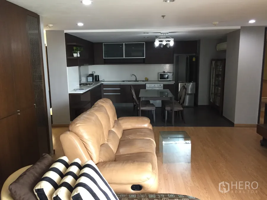 公寓 出租在Watthana, Bangkok - 开放式客厅配米色皮沙发、玻璃餐桌与深色橱柜的一体化厨房，电器齐全。