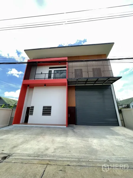 Factory for rent or sale in Lam Luk Ka, Pathum Thani - Two-storey mini factory facade with red frame, balcony, and a large gray roller shutter.