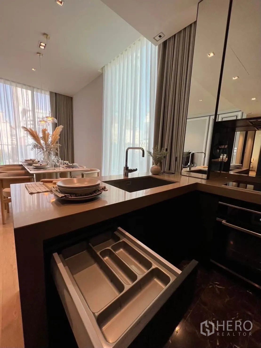 Condominium for rent in Pathum Wan, Bangkok - Kitchen detail with induction hob, sink, and open utensil drawer facing the dining area.