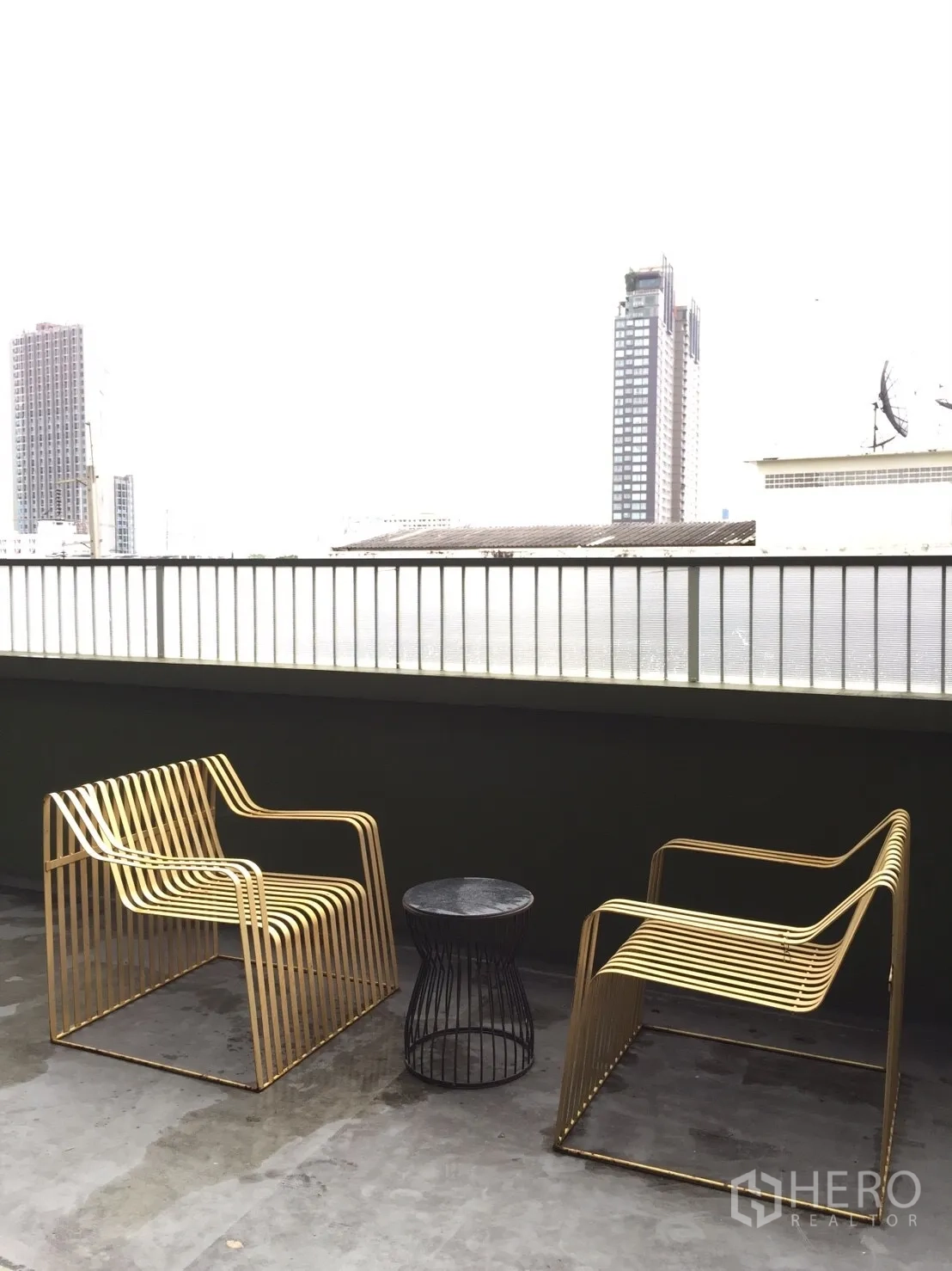 Condominium for rent or sale in Watthana, Bangkok - Private balcony with two gold metal chairs, a side table and city view.