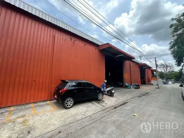คลังสินค้า ให้เช่าในBang Kapi, Bangkok - โกดังผนังเมทัลชีทสีแดง มีช่องโหลดกว้าง ประตูเปิด และที่จอดริมถนนคอนกรีต