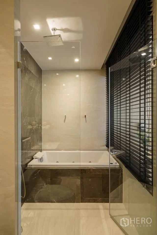 公寓 for rent in Bang Rak, Bangkok - 浴室设有玻璃干湿分离、雨淋花洒与石材包边浴缸，旁为百叶窗。