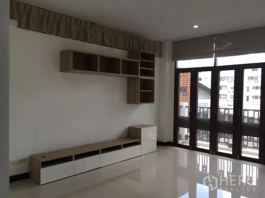 ทาวน์เฮาส์ ให้เช่าในWatthana, Bangkok - ห้องนั่งเล่นมีชั้นวางบิลท์อินและประตูกระจกสูงเปิดสู่ระเบียง