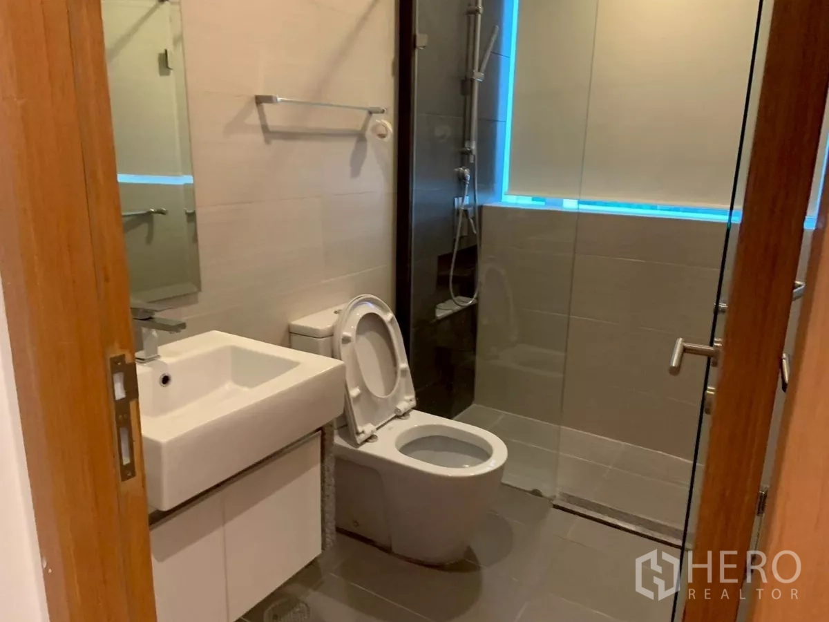 Condominium for rent in Khlong Toei, Bangkok - Shower bathroom with glass enclosure, toilet and vanity.