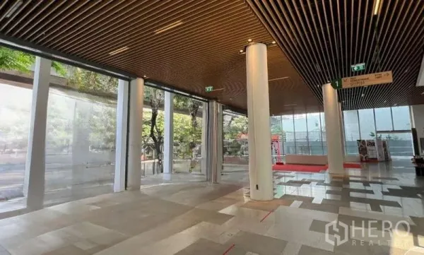 Retail Space for rent in Phaya Thai, Bangkok - Open lobby-style retail area with tall white columns, wooden slat ceiling, and expansive glass walls with street trees visible outside.