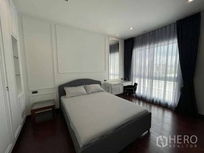 Detached House for rent or sale in Lat Krabang, Bangkok - Bright bedroom with a queen bed, desk and floor-to-ceiling curtains opening to a balcony view.