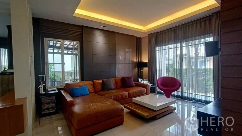 บ้าน ขายในPrawet, Bangkok - ห้องนั่งเล่น โซฟาหนังรูปตัวแอล ฝ้าหลุมไฟซ่อน และประตูกระจกกว้างออกลาน