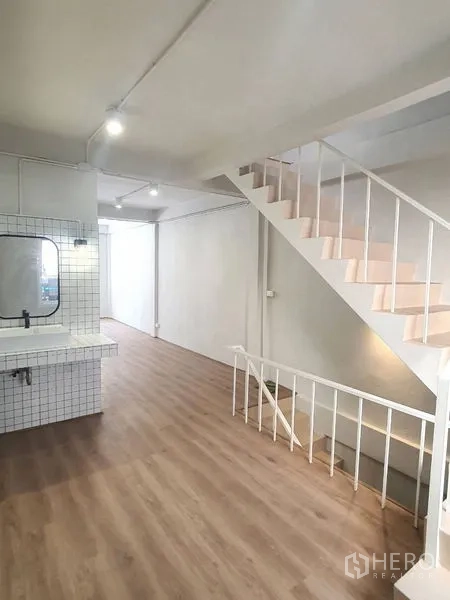 Shophouse for rent in Phra Khanong, Bangkok - Open workspace with staircase and built-in tiled sink against white walls and wood flooring.
