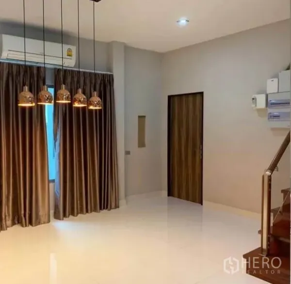 独立式住宅 出售在Mueang Pathum Thani, Pathum Thani - 明亮客厅，吊灯、落地窗帘、亮面地砖与楼梯相连。