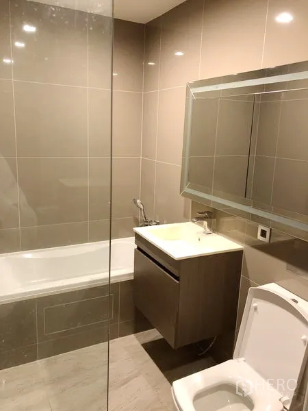 Condominium for rent in Watthana, Bangkok - Modern bathroom with bathtub, vanity, and large mirror in neutral tiles.