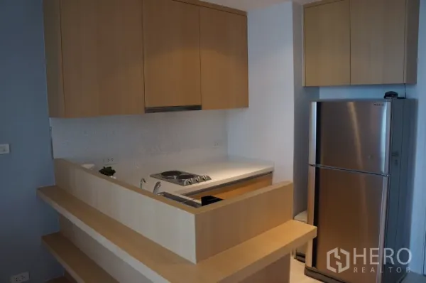 Condominium for rent in Ratchathewi, Bangkok - Modern compact kitchen with light wood cabinetry, electric hob and stainless refrigerator.
