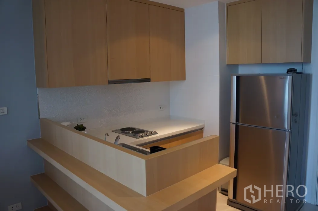 Condominium for rent in Ratchathewi, Bangkok - Modern compact kitchen with light wood cabinetry, electric hob and stainless refrigerator.