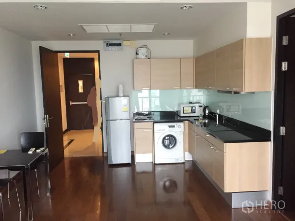 公寓 出租或出售在Pathum Wan, Bangkok - 开放式厨房，浅木橱柜、黑色台面、玻璃防溅板，配洗衣机与用餐区。
