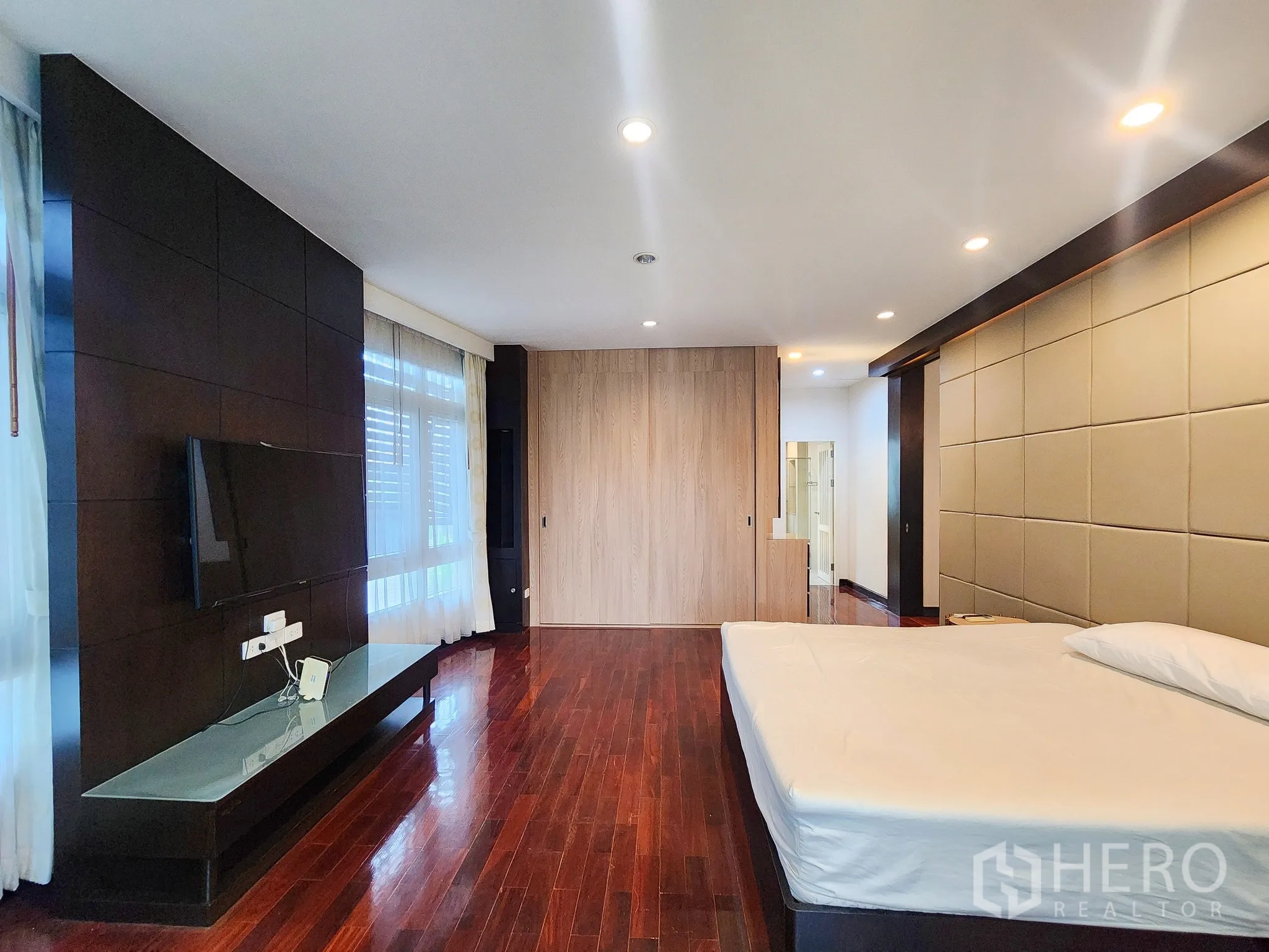 Detached House for rent in Bang Kapi, Bangkok - Large master bedroom with TV wall, polished wood floors and wide windows.