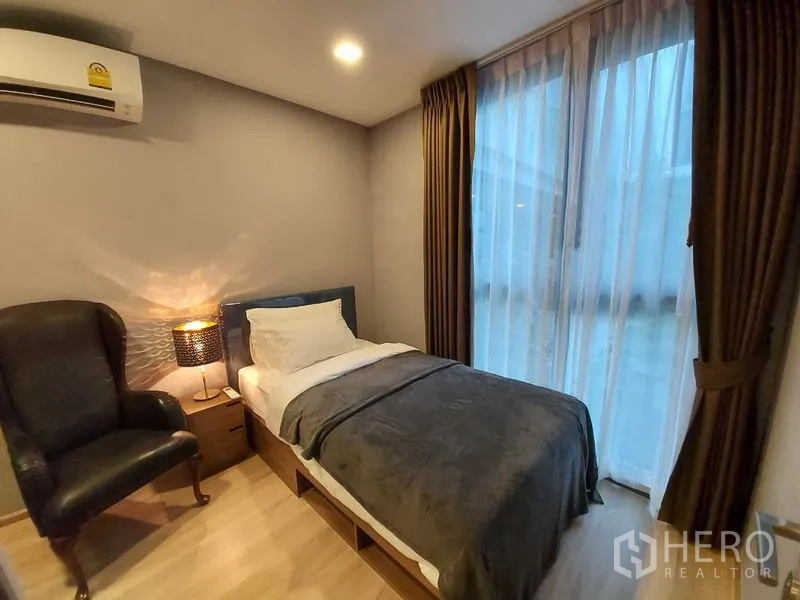 公寓 出租或出售在Watthana, Bangkok - 次卧配单人床、扶手椅与落地窗帘。