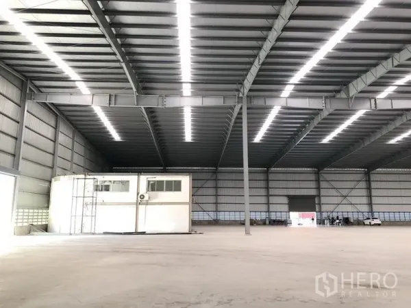Factory for rent in Bang Phli, Samut Prakan - Vast high-clear warehouse interior with steel trusses, skylight strips, and a small mezzanine office.