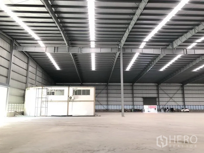 Factory for rent in Bang Phli, Samut Prakan - Vast high-clear warehouse interior with steel trusses, skylight strips, and a small mezzanine office.