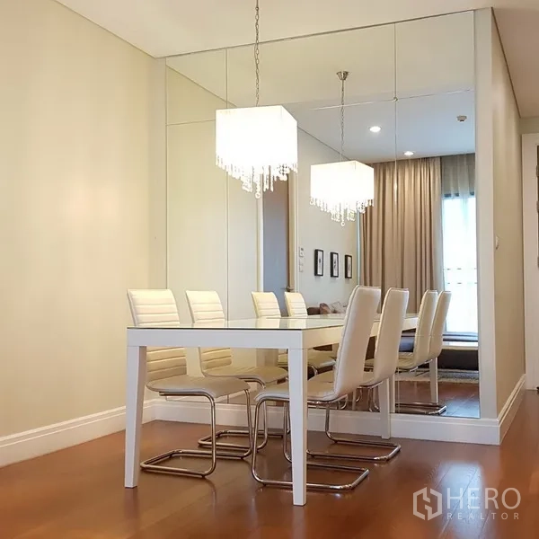 Condominium for rent in Khlong Toei, Bangkok - Dining space with white table and chairs, mirrored wall and crystal pendant lighting.