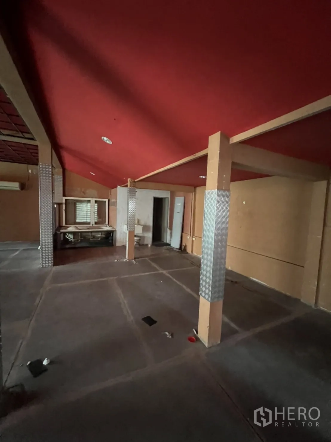 Shophouse for rent in Watthana, Bangkok - Spacious hall with support columns wrapped in checker-plate metal and a red ceiling.