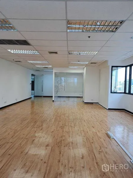 Office Space for rent in Bang Rak, Bangkok - Open workspace with ceiling grid lights, wood floors and corner windows bringing in natural light.