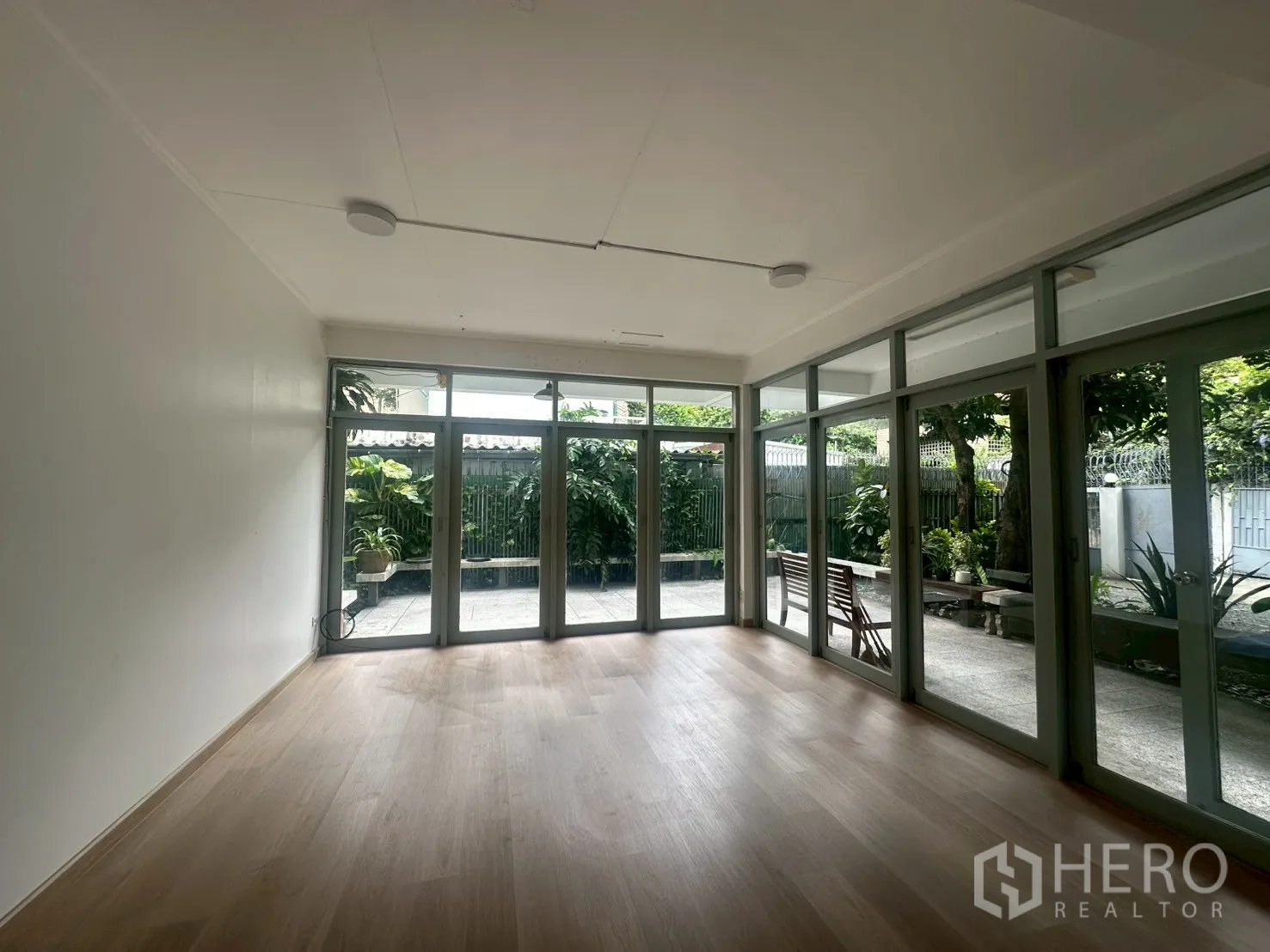 独立式住宅 出租在Watthana, Bangkok - 明亮客厅，浅色木地板，整面落地玻璃门通向露台。