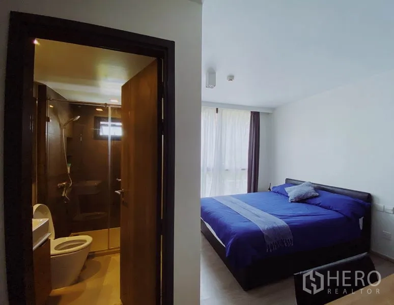 Condominium for rent in Pathum Wan, Bangkok - Master bedroom with blue bedding and ensuite bathroom behind a wooden door.