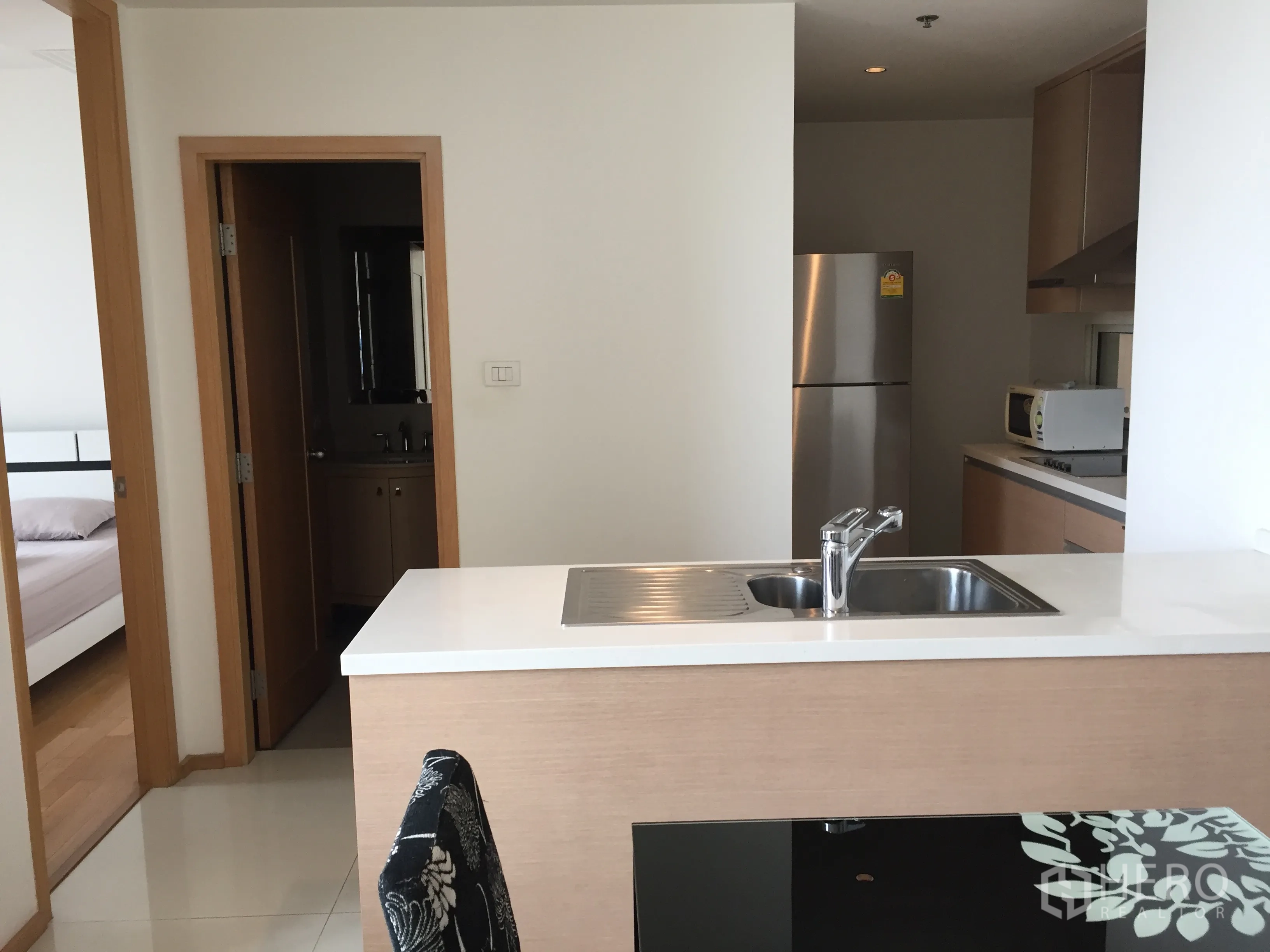 Condominium for rent in Sathon, Bangkok - Modern kitchen with island sink, stone countertop, stainless refrigerator and built-in cabinets leading toward bedrooms and bathroom.