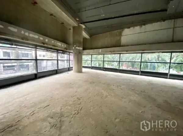 Retail Space for rent - Spacious concrete interior with central column and wraparound windows bringing natural light.