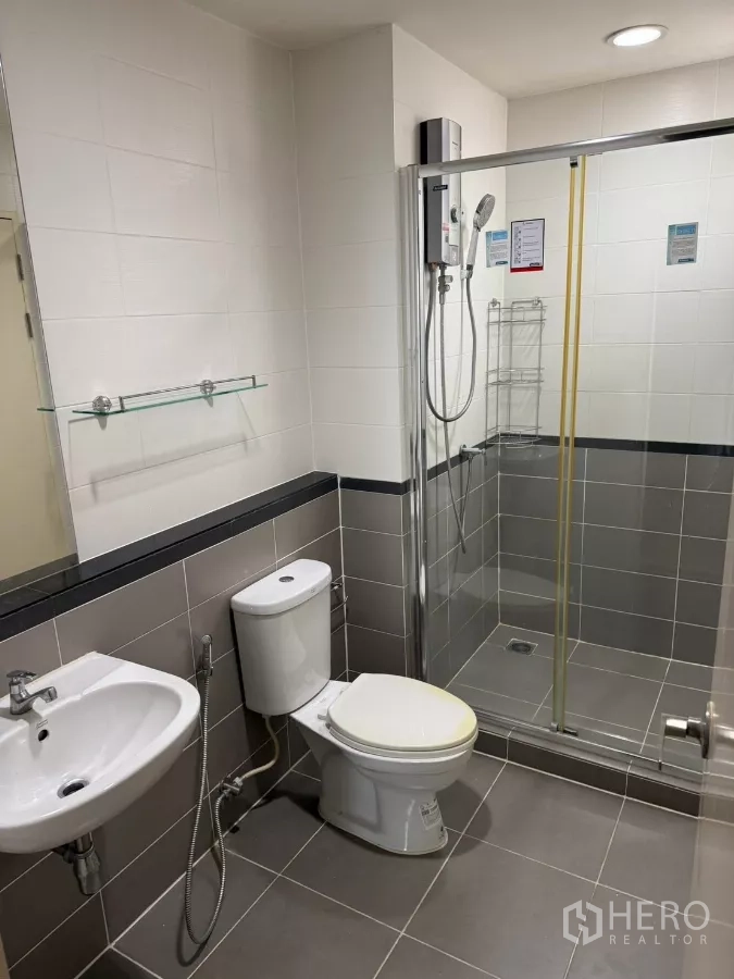 Townhouse for rent in Suan Luang, Bangkok - Modern bathroom with glass shower enclosure, water heater and gray tiles.