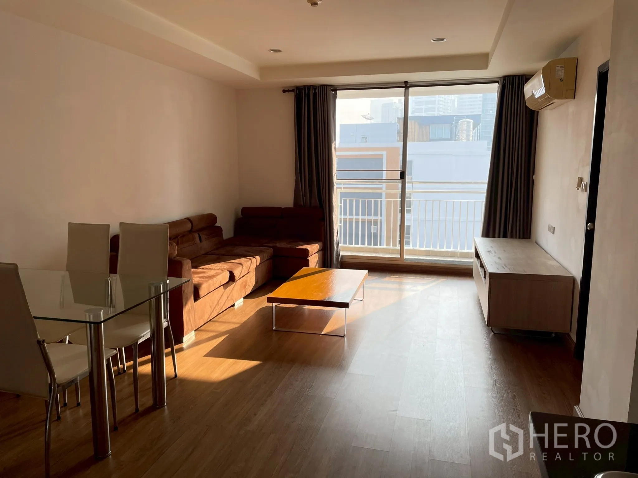 Apartment for rent in Khlong Toei, Bangkok - Spacious lounge with brown sectional sofa, coffee table, and balcony access.