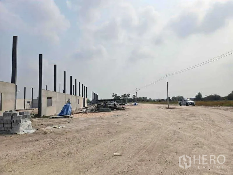 货栈 出售在Ban Bueng, Chon Buri - 仓库工地旁宽阔的碎石场地与出入口，道路有电线杆，周边开阔的田野。
