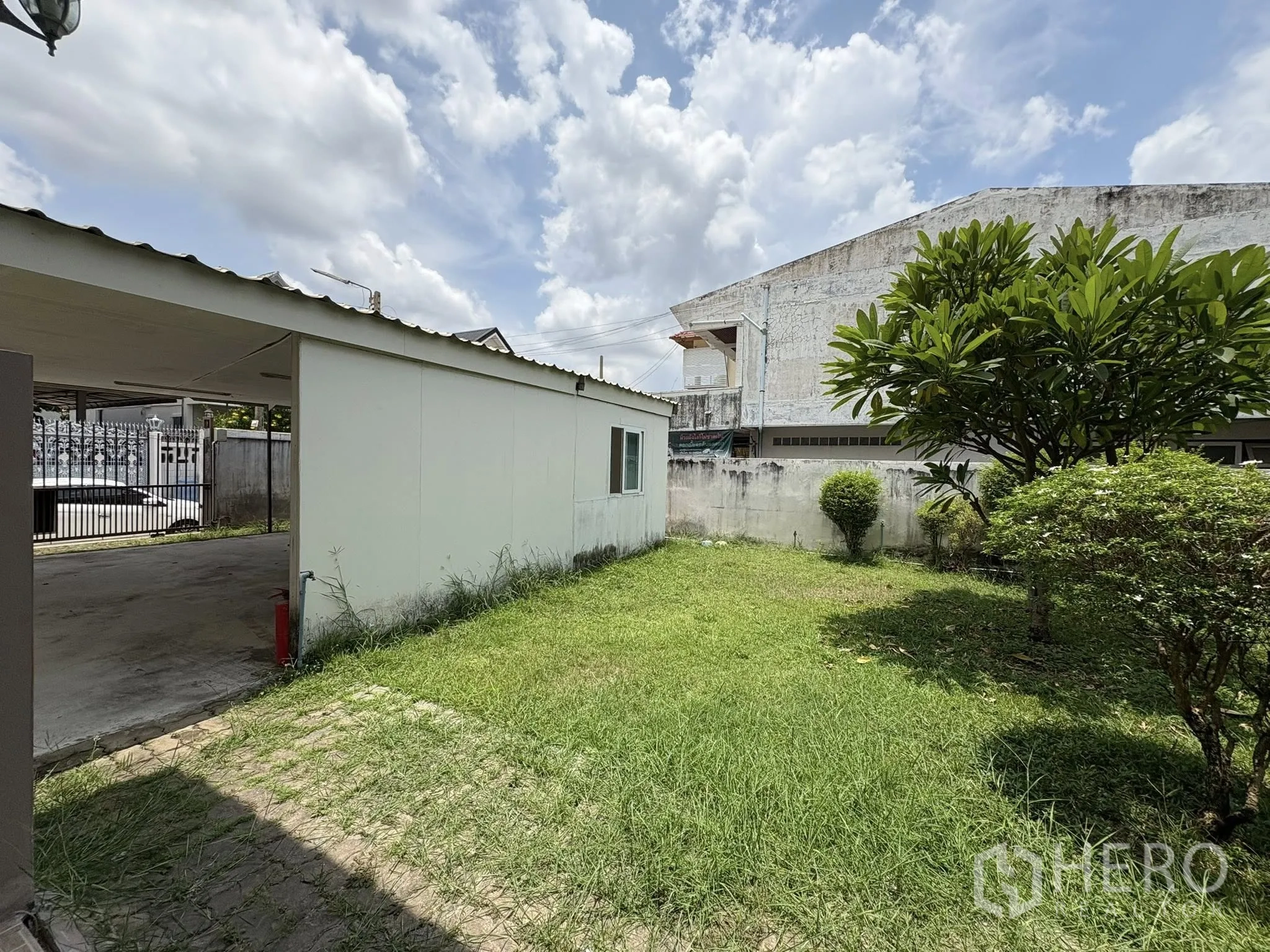 独立式住宅 出售在Phra Khanong, Bangkok - 侧院草坪、白色附属墙体与小灌木。