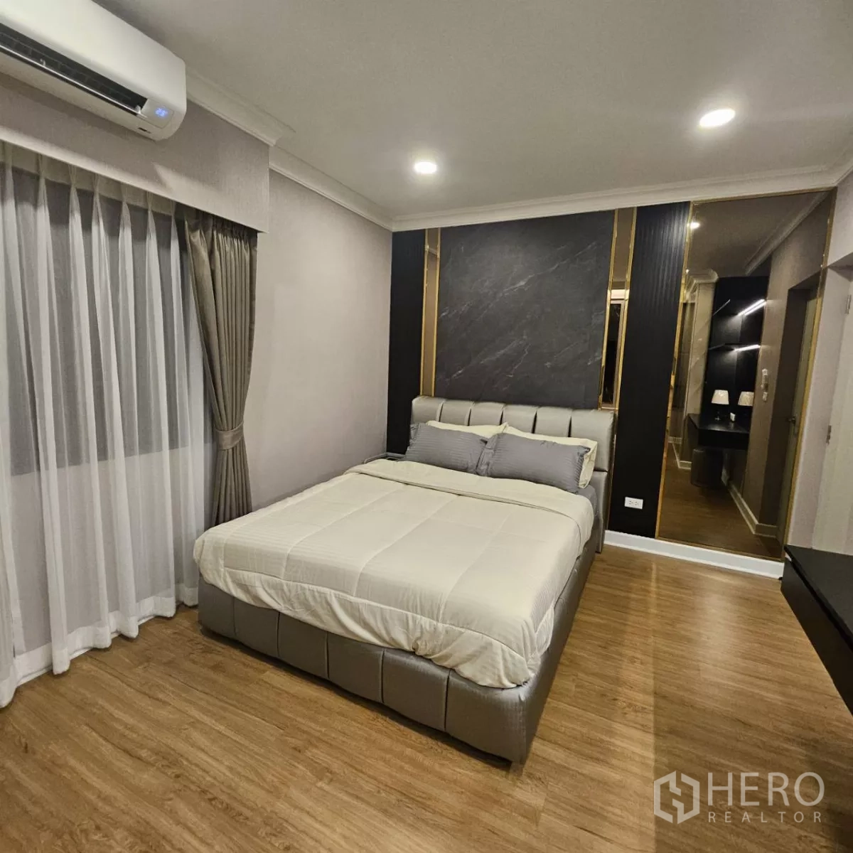 独立式住宅 出租在Bang Phli, Samut Prakan - 卧室配软包床、木地板、窗帘与带金色饰条的特色背景墙及梳妆台。
